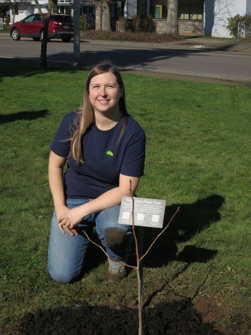 Lead organizer Reilly Newman kneels behind the tree and informational plaque